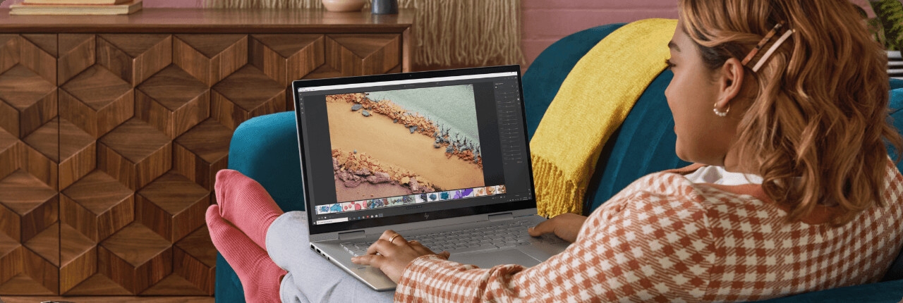 شابة تجلس على الأريكة وتحرر صورة باستخدام كمبيوتر محمول HP ENVY x360
